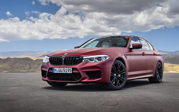 A matte red BMW M5 sports car parked on an open road under a cloudy sky, captured in 4K Ultra HD for a PC desktop wallpaper.