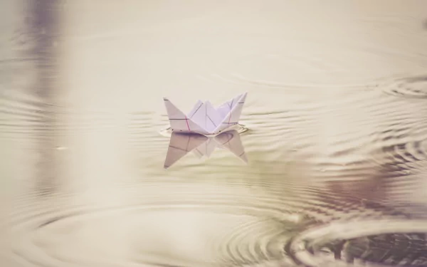 HD PC desktop wallpaper: an origami paper boat floating on calm water with gentle ripples around the man-made craft.