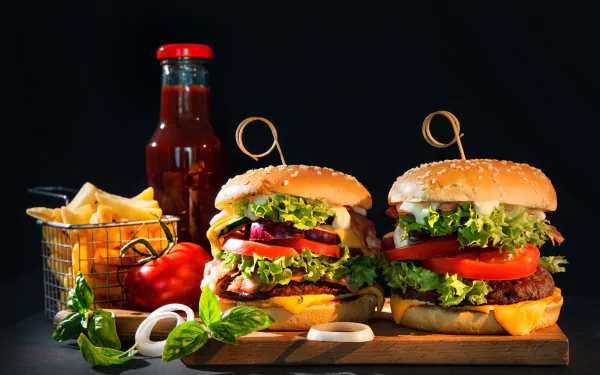 A vibrant still life featuring two delicious burgers topped with fresh vegetables, a side of crispy French fries, and a bottle of ketchup, all set against a dark background.