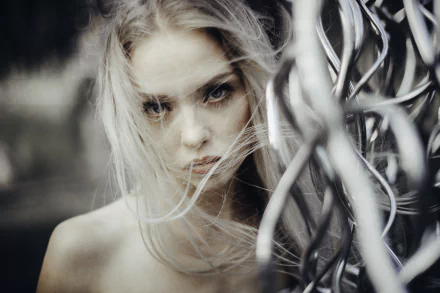 Close-up HD desktop wallpaper of a blonde woman with blue eyes staring intensely, her hair softly flowing around her face against a blurred background.