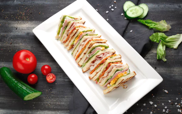 HD PC desktop wallpaper featuring a neatly arranged sandwich platter on a white rectangular plate with fresh vegetables on a dark wooden surface.