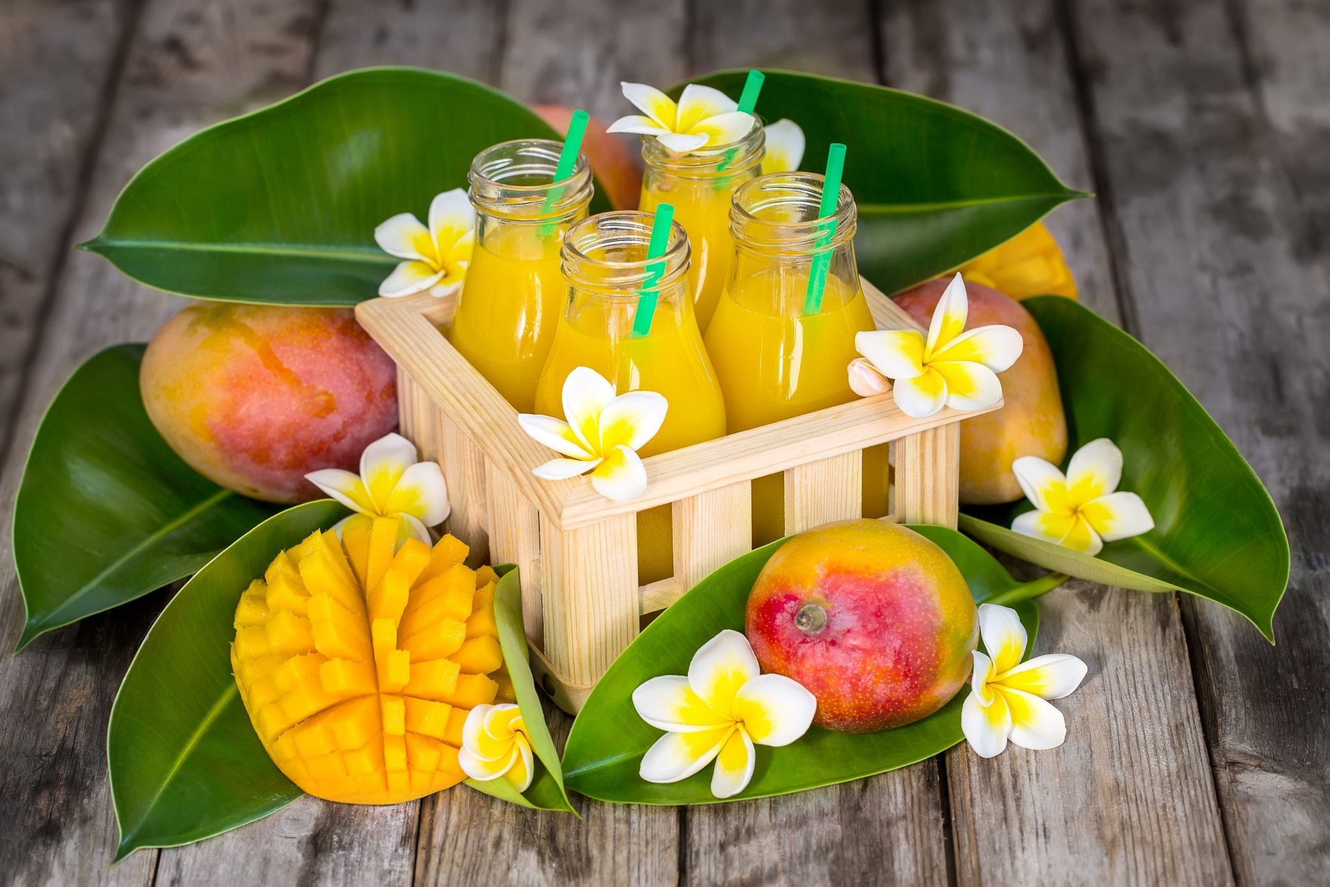 5K Ultra HD PC desktop wallpaper background — still-life of mango fruit: sliced mango and whole fruit with glass jars of mango drink, straws and tropical flowers on green leaves.