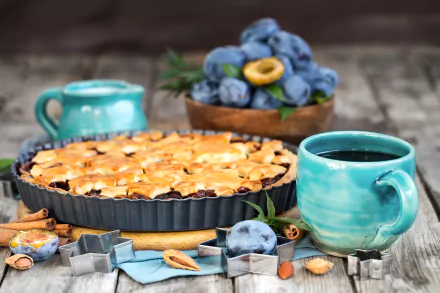 A 4K Ultra HD still life featuring a plum pie, fresh plums in a bowl, a steaming cup of coffee in a turquoise cup, and pastry tools arranged on a rustic wooden table.