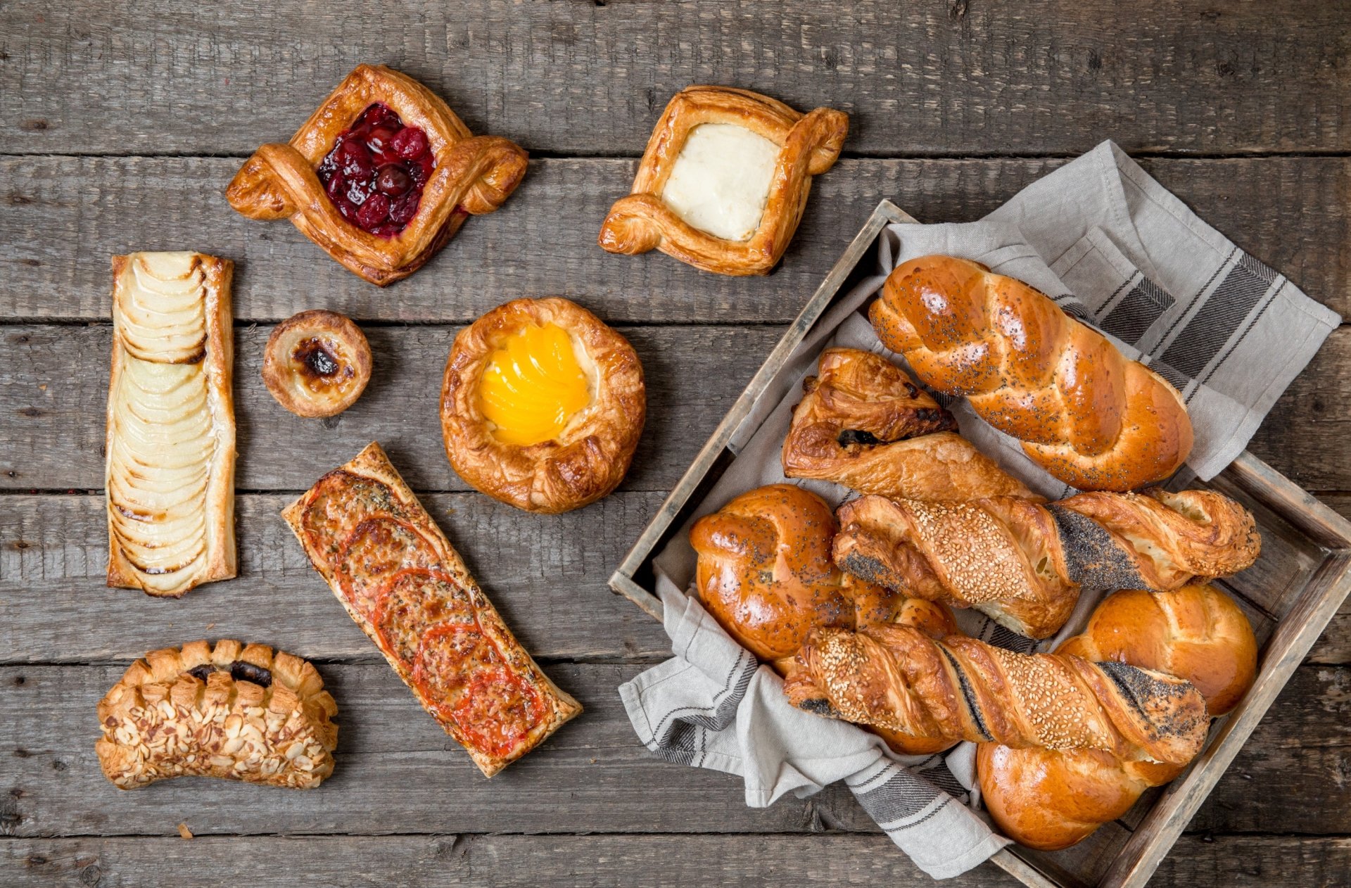 HD desktop wallpaper showcasing a variety of golden viennoiserie baked goods arranged on a rustic wooden surface, highlighting artisanal baking and fresh food in a still life composition.