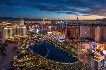 A stunning night view of Las Vegas, showcasing vibrant skyscrapers and a bustling cityscape illuminated by colorful lights. The iconic Ferris wheel adds to the lively atmosphere.