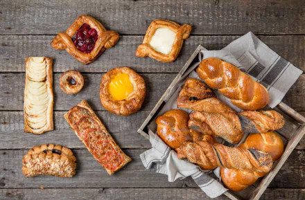 HD desktop wallpaper showcasing a variety of golden viennoiserie baked goods arranged on a rustic wooden surface, highlighting artisanal baking and fresh food in a still life composition.