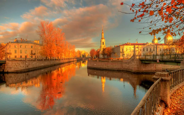 HD desktop wallpaper showcasing autumn colors along a river with historic buildings and cityscape of Saint Petersburg, Russia under a dramatic sky.