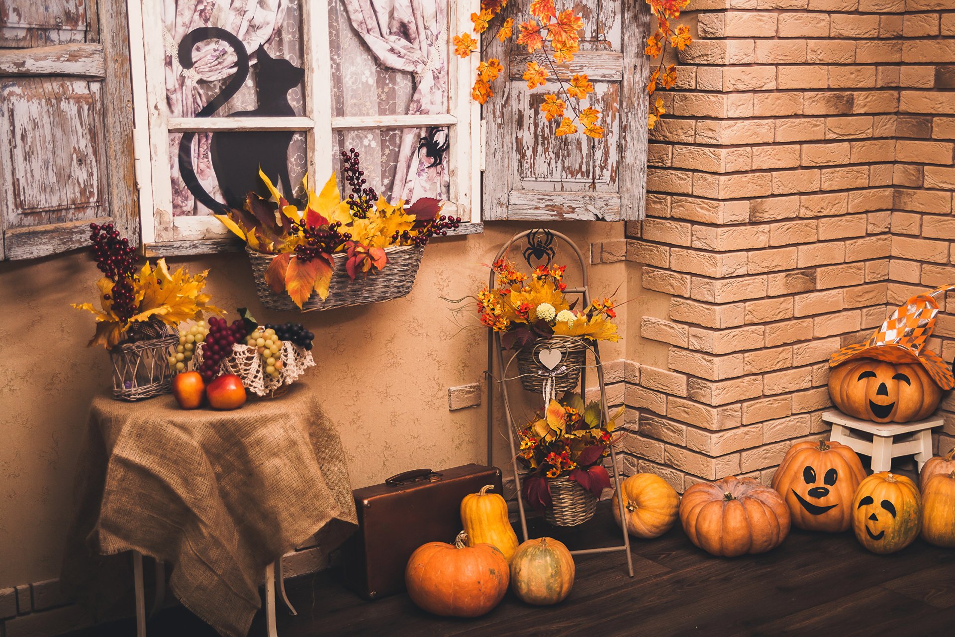 HD PC desktop wallpaper featuring a cozy Halloween holiday scene with pumpkins, autumn leaves, and rustic decorations by a brick wall and window.