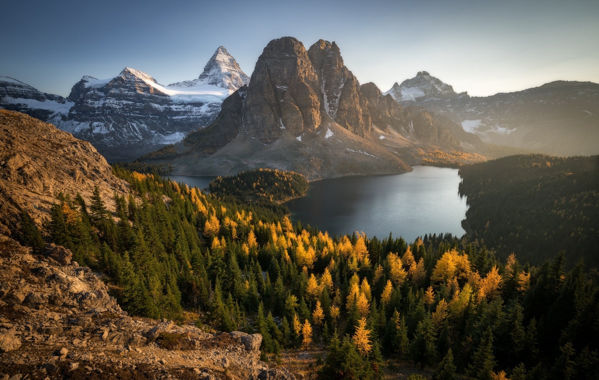 HD PC desktop wallpaper featuring a serene mountain landscape with a forest of autumn trees surrounding a calm lake at sunrise.