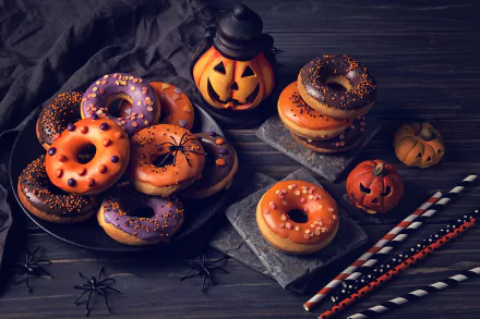 HD desktop wallpaper featuring Halloween-themed doughnuts in orange and purple, decorated with sprinkles, surrounded by small pumpkins and festive straws on a dark wooden surface.