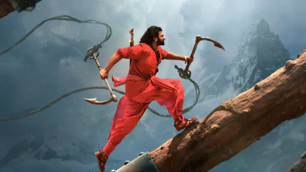 HD desktop wallpaper from the movie Baahubali 2: The Conclusion, featuring a dynamic action scene of a warrior in red attire climbing a tree trunk with weapons against a mountainous background.