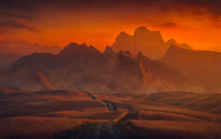 HD desktop wallpaper depicting a serene summer sunset over a dirt road and field, set against a backdrop of majestic mountains.