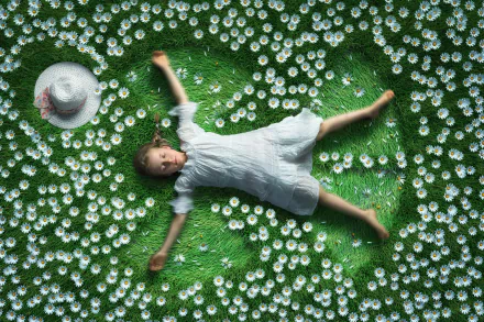 HD PC wallpaper of a little girl child lying down on green grass dotted with daisies, white dress and straw hat beside her — bright, whimsical photography background.