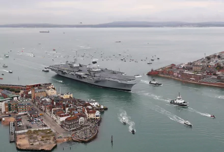 HD desktop wallpaper showing the HMS Queen Elizabeth (R08) aircraft carrier, a prominent military warship, navigating through a busy coastal harbor.