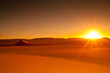 HD desktop wallpaper of a sunset over the orange sands of the Sahara Desert in Algeria's Tassili N'Ajjer region, with the Hoggar Mountains in the background. Beautiful natural landscape in Africa.