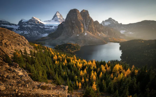 HD PC desktop wallpaper featuring a serene mountain landscape with a forest of autumn trees surrounding a calm lake at sunrise.