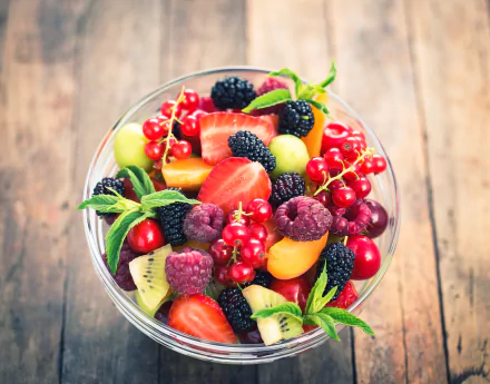 A vibrant bowl of mixed fruit featuring blackberries, currants, strawberries, and raspberries. The image is an HD desktop wallpaper and background showcasing fresh, colorful fruit on a wooden surface.