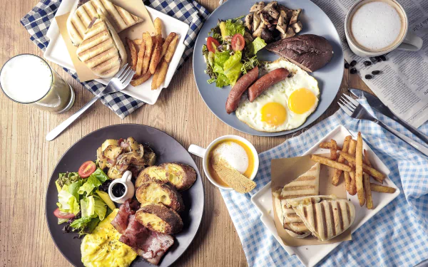 HD desktop wallpaper of a breakfast still life featuring eggs, sausage, salad, fries, toast, and a cup of milk on a wooden table.