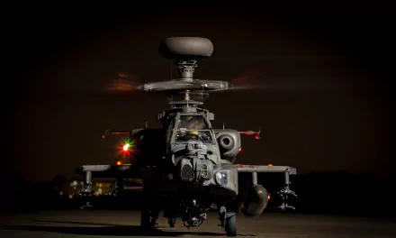 HD desktop wallpaper featuring a Boeing AH-64 Apache attack helicopter illuminated against a dark background, showcasing its military design and advanced aircraft technology.
