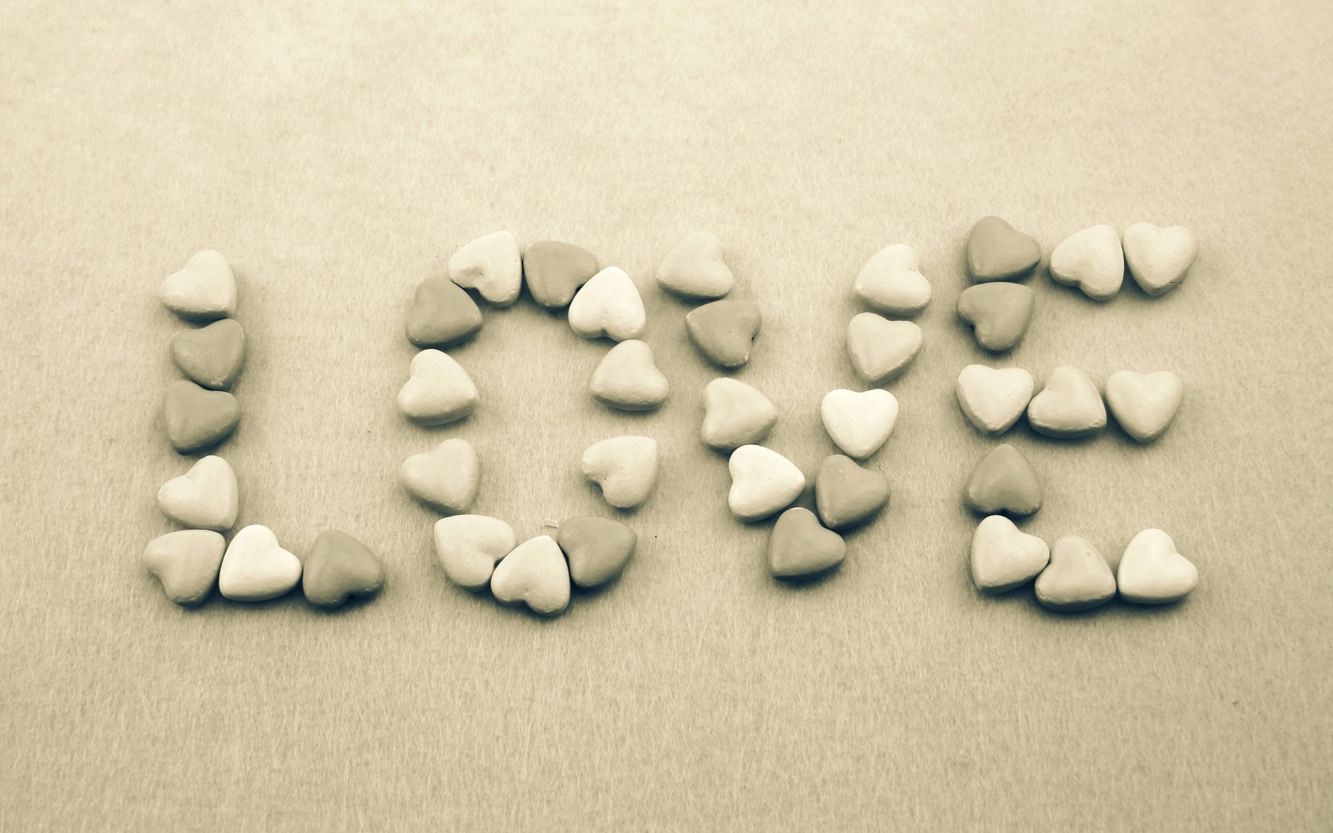HD desktop wallpaper featuring the word 'LOVE' spelled out with heart-shaped stones on a beige background. Artistic and warm, this image embodies the concept of love and nature.