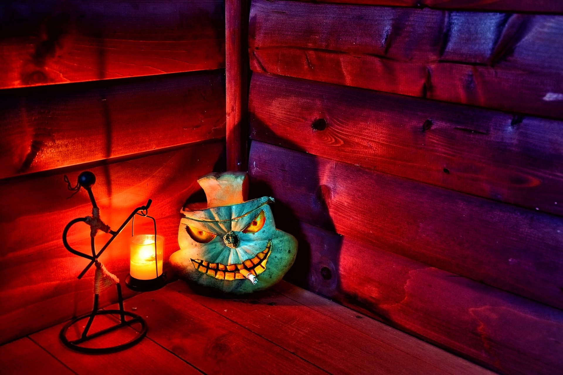 A Halloween-themed HD PC wallpaper featuring a glowing jack-o'-lantern candle holder and a lit candle on a wooden floor with a cigarette holder nearby.