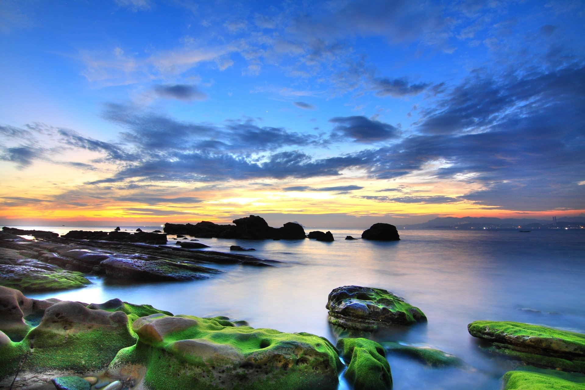 HD desktop wallpaper featuring a serene ocean horizon under a vibrant sky filled with clouds, showcasing nature’s tranquil beauty with moss-covered rocks in the foreground.