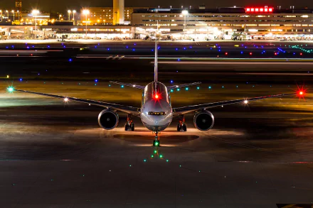 An HD desktop wallpaper of a passenger plane on a runway at night, with airport lights in the background, showcasing the aircraft in a vibrant and dynamic airport setting.