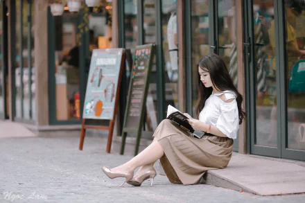 Asian brunette model in high heels reading on a city sidewalk bench in front of a café. HD desktop wallpaper and background.