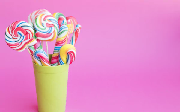 A vibrant HD desktop wallpaper featuring colorful spiral lollipops arranged in a green cup against a solid pink background.
