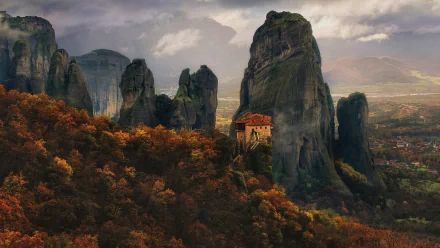 HD desktop wallpaper of Meteora, Greece, showcasing towering mountain cliffs, a religious monastery nestled among the forest, and a dramatic sky in autumn fall colors.