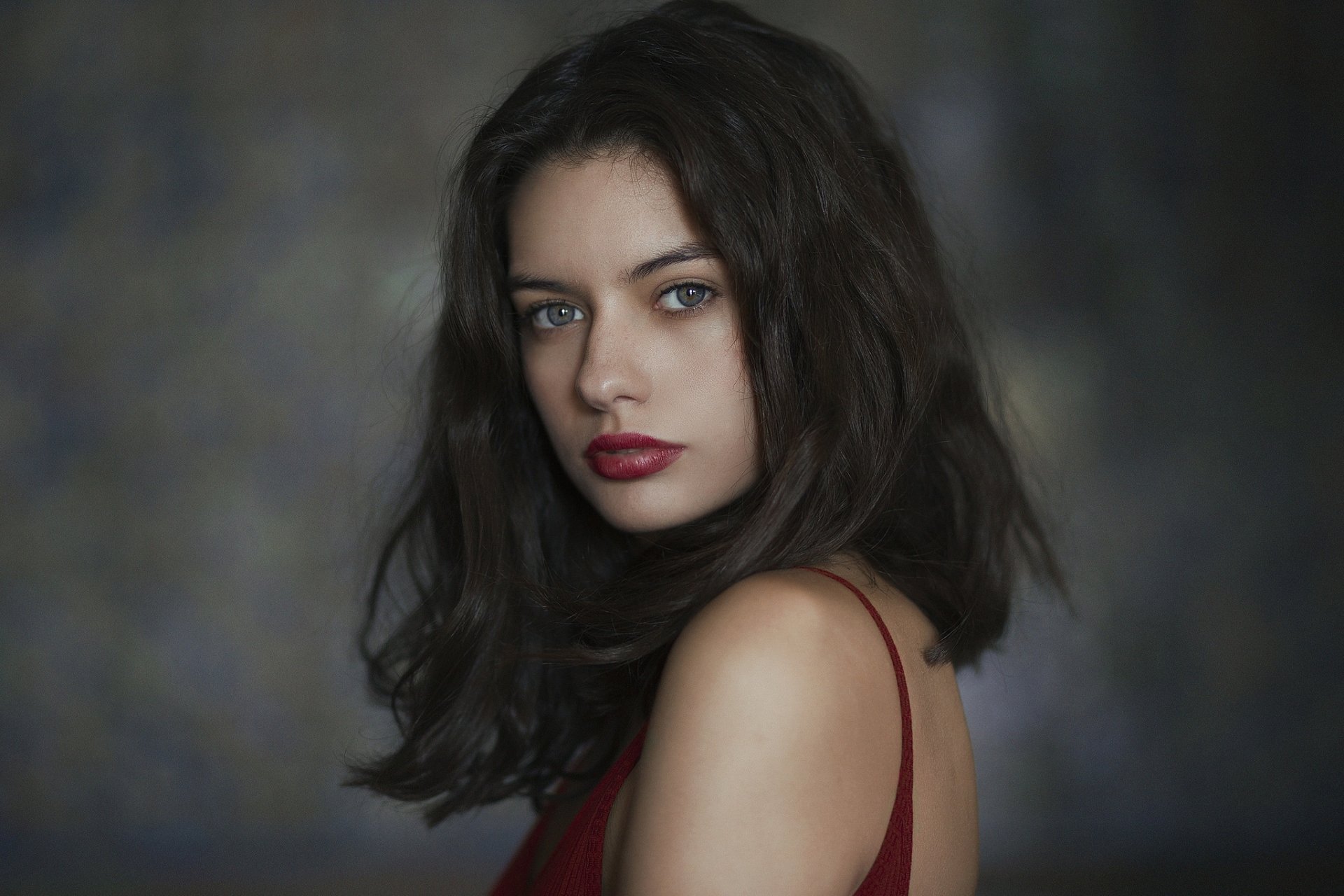 HD desktop wallpaper of a brunette woman with blue eyes and red lipstick, featuring a close-up portrait against a dark, blurred background.