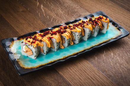 HD desktop wallpaper featuring a vibrant sushi roll with seafood, fish, and rice artfully arranged on a ceramic plate against a wooden surface background.