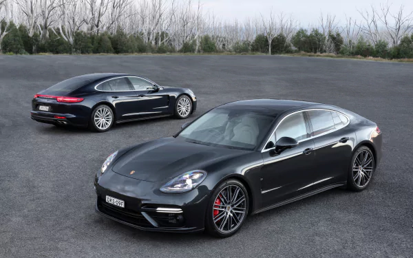 A black Porsche Panamera displayed as an HD PC desktop wallpaper, showcasing two sleek vehicles on an open paved surface with trees in the background.