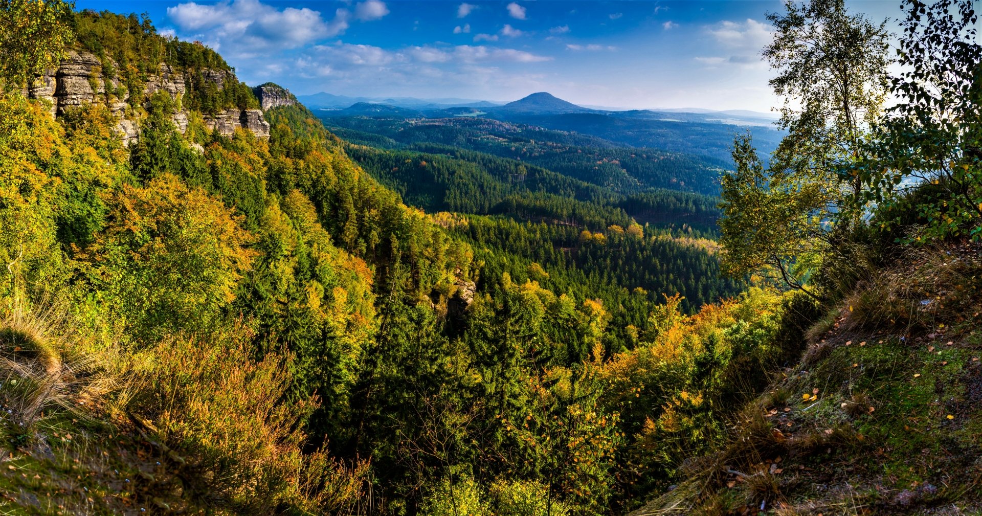HD desktop wallpaper featuring a stunning fall landscape with colorful forests blanketing the mountains and valleys under a clear blue sky.