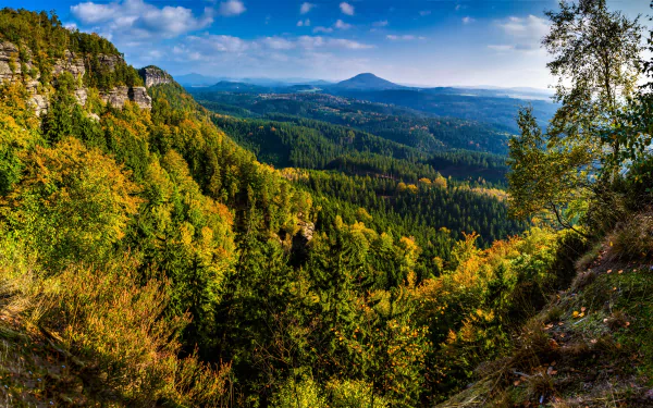 HD desktop wallpaper featuring a stunning fall landscape with colorful forests blanketing the mountains and valleys under a clear blue sky.