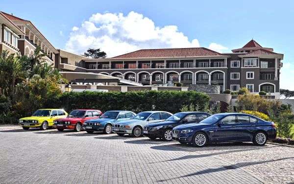 A lineup of colorful BMW cars, including a standout yellow vehicle, parked in front of a large, elegant building, captured in 4K Ultra HD.