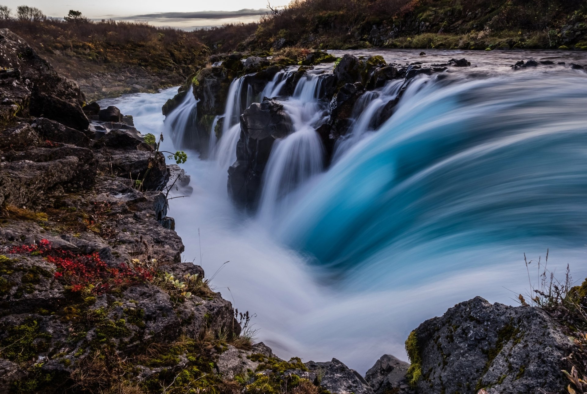 HD PC desktop wallpaper: foam-capped turquoise waterfall cascading between rocky, mossy cliffs; long-exposure silky water and mist in a rugged natural landscape.