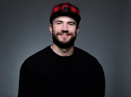 HD desktop wallpaper of a man in a black shirt and red plaid hat smiling against a grey background.