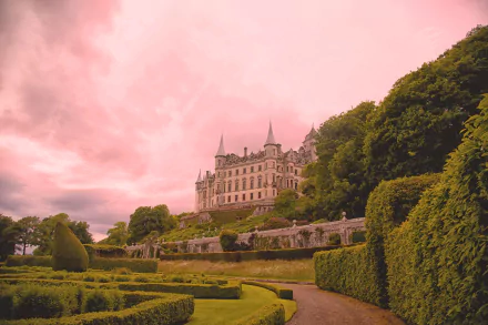 Wide HD desktop wallpaper of man-made Dunrobin Castle in Scotland rising above formal manicured terraced gardens and hedgerows under a dramatic pink sky.