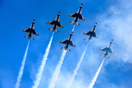 Formation of United States Air Force Thunderbirds flying General Dynamics F-16 Fighting Falcons, releasing smoke trails during an air show against a clear blue sky.