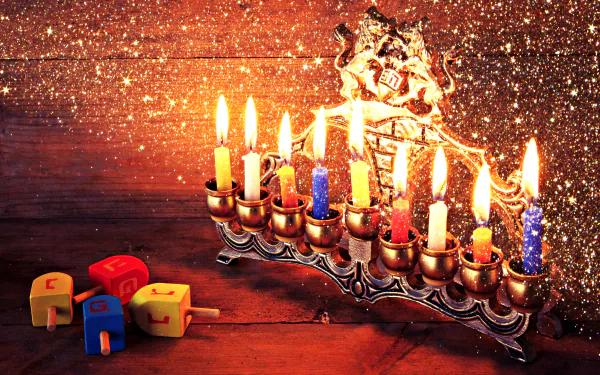 HD desktop wallpaper featuring a glowing Hanukkah menorah with lit candles and colorful dreidels on a wooden surface, surrounded by festive golden sparkles.
