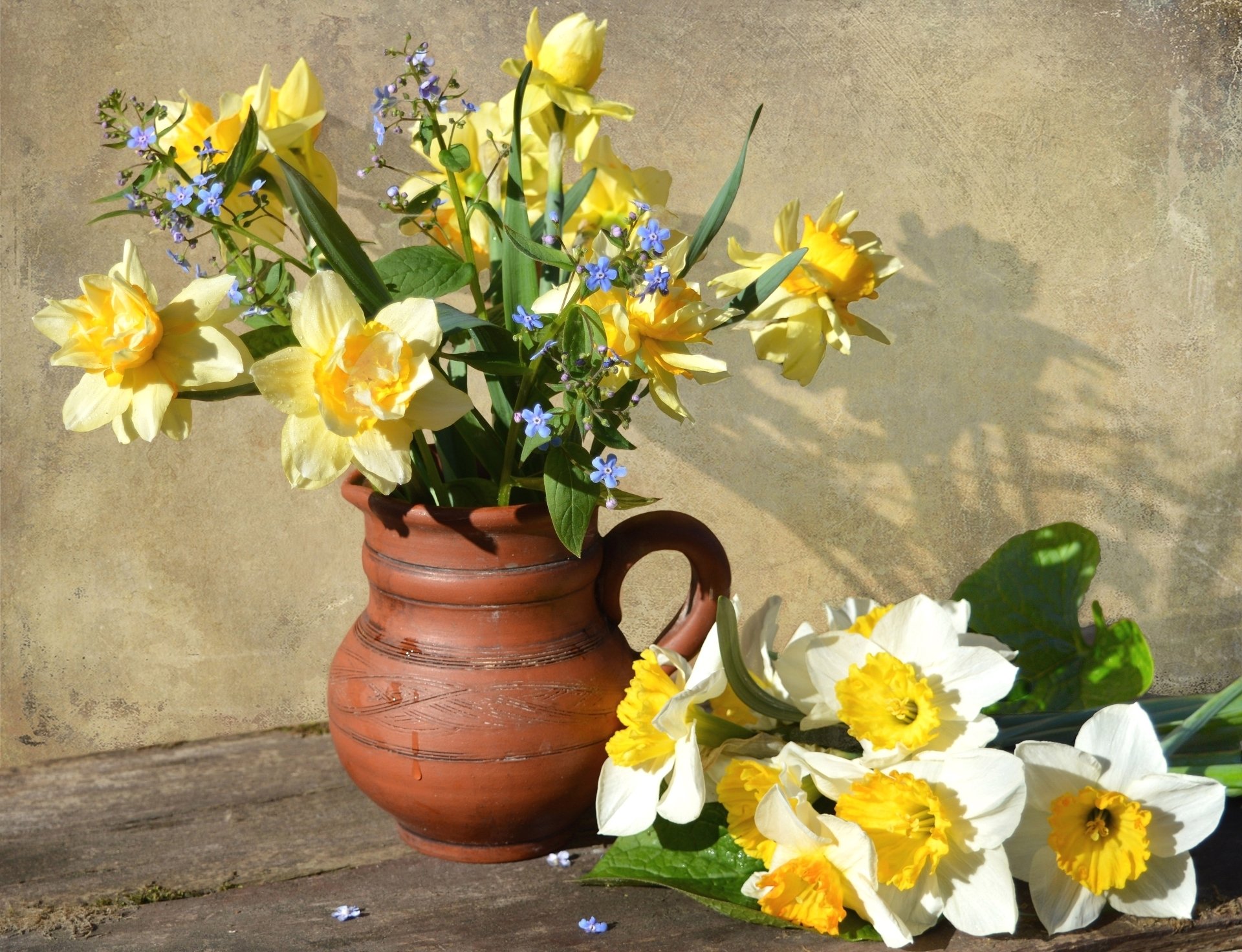 A still life HD desktop wallpaper featuring yellow and white daffodils in a rustic vase against a textured wall, showcasing vibrant floral photography.