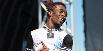 HD desktop wallpaper of a smiling person with dyed dreadlocks, performing on stage, evoking a lively musical atmosphere.