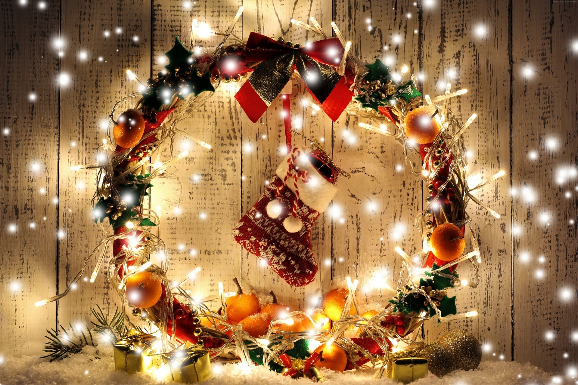 A glowing holiday wreath decorated with apricots, a red stocking, and warm lights hangs on a wooden background, captured in 4K Ultra HD for a festive Christmas PC wallpaper.