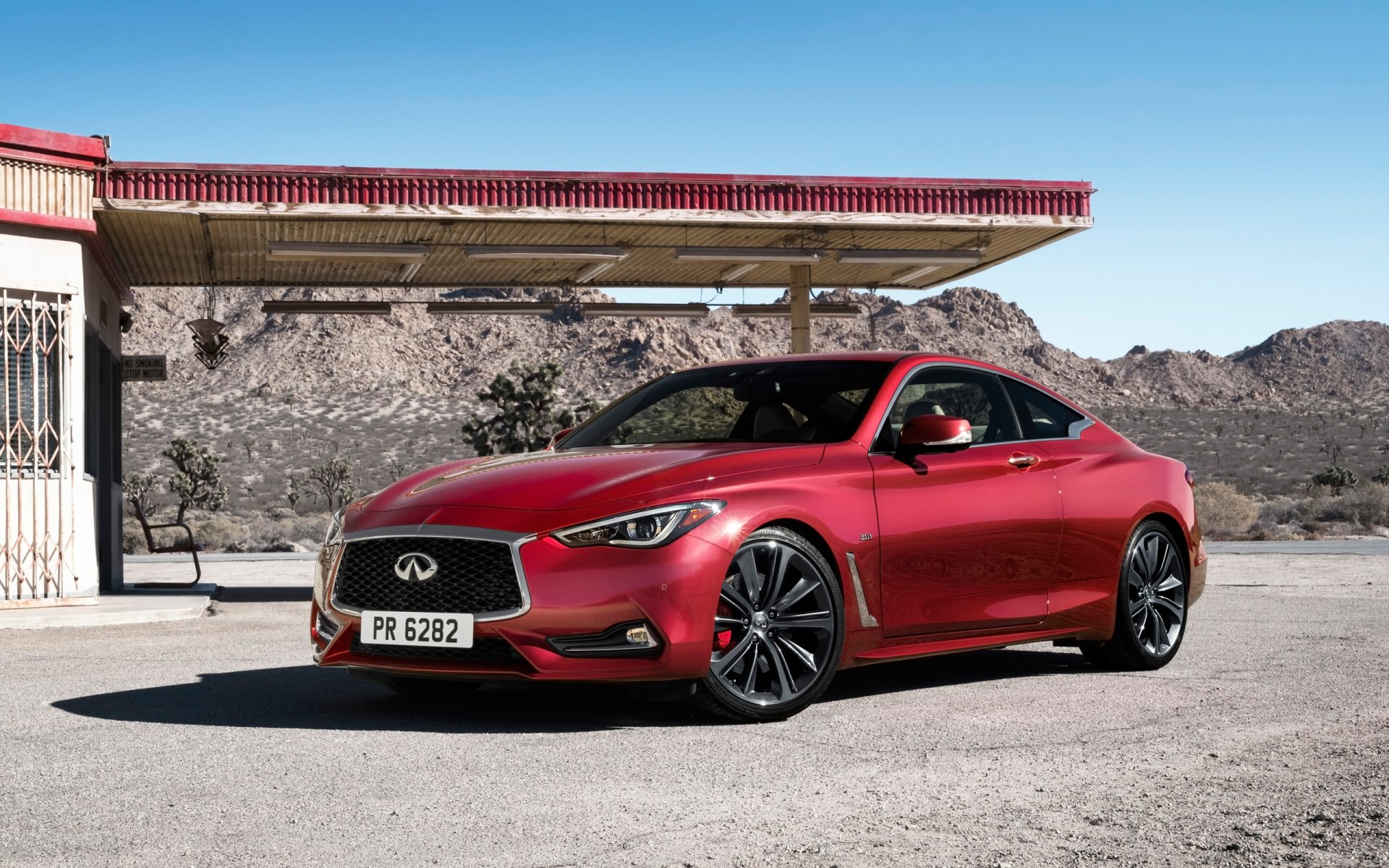 Red Infiniti Q60 coupe parked beside a vintage gas station in a desert setting under a clear blue sky — 2K Quad HD PC desktop wallpaper background.