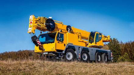 HD desktop wallpaper featuring a bright yellow Liebherr construction crane vehicle set against a clear blue sky and grassy field background.