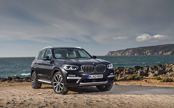 BMW X3 SUV parked on a rocky coastal shore with dramatic sky and sea — 4K Ultra HD PC desktop wallpaper of a BMW vehicle.