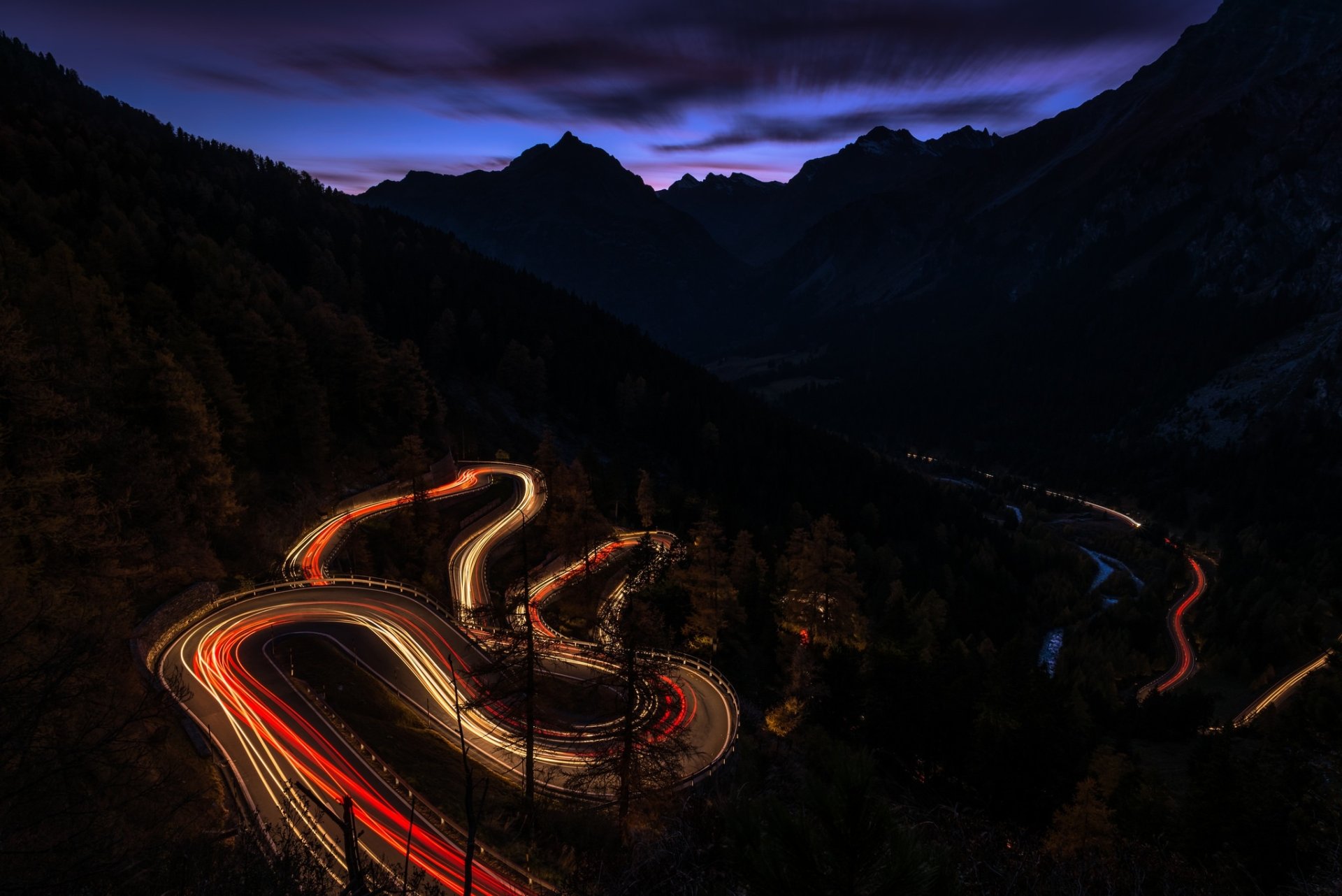 A night-time time-lapse of a winding man-made road through mountainous terrain, captured in HD for a PC desktop wallpaper and background.
