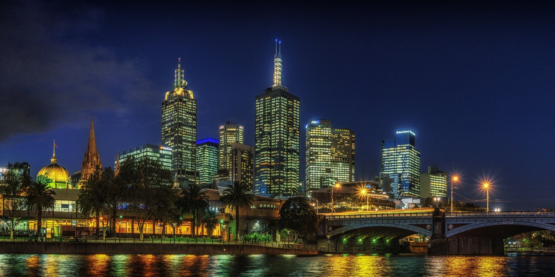 Night view of Melbourne’s illuminated skyscrapers and bridge reflecting on the river, showcasing the city’s vibrant man-made architecture in Australia.