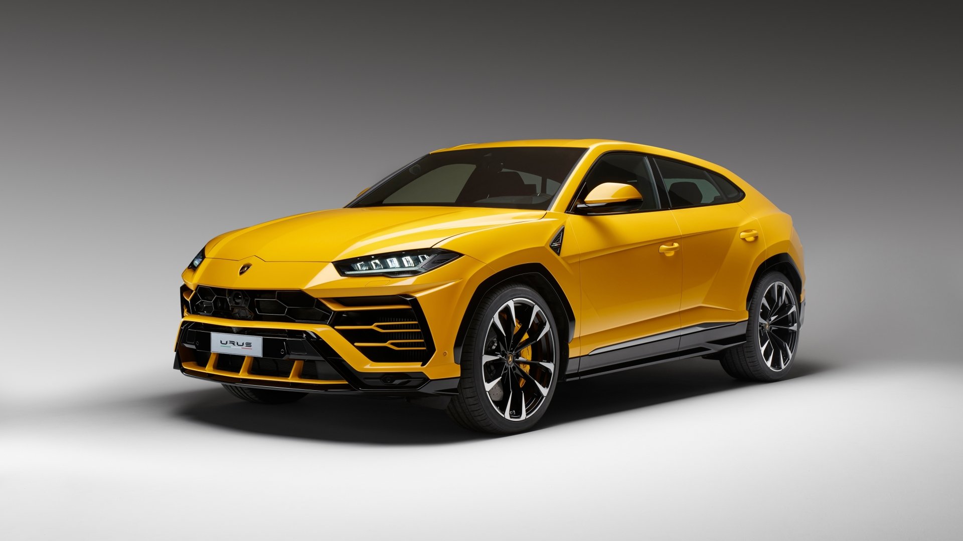 A vibrant yellow Lamborghini Urus SUV showcased in a high-definition desktop wallpaper, set against a gradient grey background.